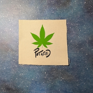 Puede incluir: Un parche de tela beige con una hoja de marihuana verde y la palabra "Pothead" escrita en cursiva negra debajo.