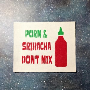 May include: A white canvas patch with the text "Porn & Sriracha Don't Mix" in green and red lettering. A red and green sriracha bottle is pictured to the right of the text.