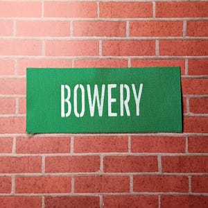 May include: A green fabric patch with the word "BOWERY" printed in white letters.