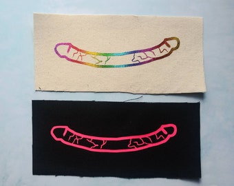 May include: Two fabric patches with an outline of a banana. The top patch is white with a rainbow colored banana. The bottom patch is black with a hot pink banana.