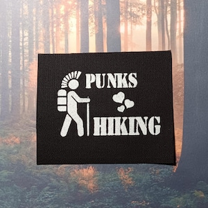 Op de afbeelding: Zwarte patch met witte tekst die "Punks ♥ Hiking" zegt. Een wit stickfiguurtje met een rugzak en een mohawk loopt links van de tekst.