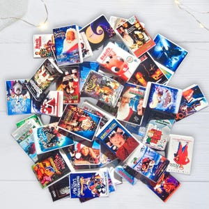 K&ouml;nnte beinhalten: Eine Ansammlung von Miniatur-VHS-Kassetten mit Weihnachts- und Urlaubsfilmen. Zu den Titeln geh&ouml;ren "Kevin &ndash; Allein zu Haus", "Santa Clause" und "Rudolph". Die Kassetten sind auf einer wei&szlig;en Oberfl&auml;che angeordnet, wobei sich einige &uuml;berlappen.