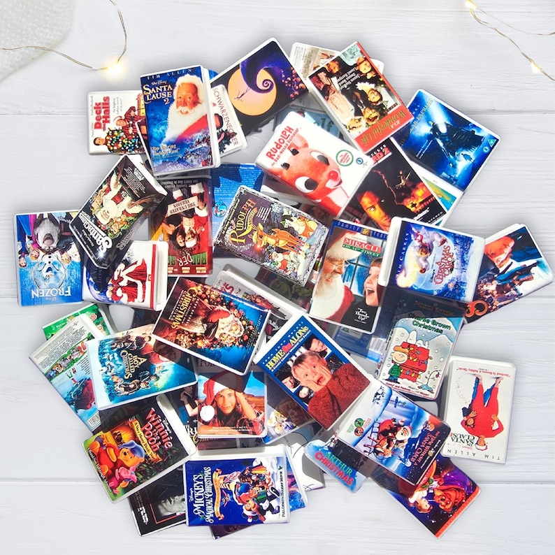 K&ouml;nnte beinhalten: Eine Ansammlung von Miniatur-VHS-Kassetten mit Weihnachts- und Urlaubsfilmen. Zu den Titeln geh&ouml;ren "Kevin &ndash; Allein zu Haus", "Santa Clause" und "Rudolph". Die Kassetten sind auf einer wei&szlig;en Oberfl&auml;che angeordnet, wobei sich einige &uuml;berlappen.