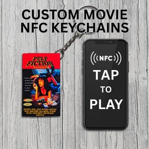Może przedstawiać: Niestandardowy brelok do filmu z plakatem filmu Pulp Fiction, połączony ze srebrnym łańcuchem i telefonem wyświetlającym "TAP TO PLAY" ze symbolem NFC. Brelok jest prostokątny z czerwonym tłem.