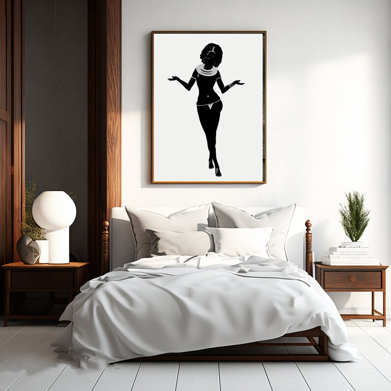 May include: A black and white silhouette of a woman wearing a necklace and a skirt, standing with her arms outstretched. The silhouette is framed in a wooden frame and is hanging on a white wall above a bed with white bedding.