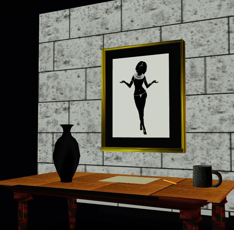 May include: A framed black and white silhouette of a woman wearing a necklace and a skirt, standing with her arms outstretched. The frame is gold and the background is a brick wall. A black vase and a brown mug are on a wooden table in the foreground.