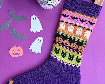May include: A purple knit sock with a Halloween-themed pattern featuring bats, ghosts, and jack-o'-lanterns. The sock is displayed on a wooden hanger against a purple background, with decorative cutouts of bats, ghosts, and a pumpkin.