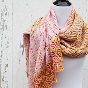 May include: A pink and yellow knitted shawl with a lacy pattern. The shawl is draped over a white mannequin.