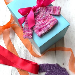 A pink miniature hand knit sweater adorning a gift with a bright pink bow.