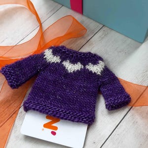 A purple miniature hand knit sweater used as a gift card holder.