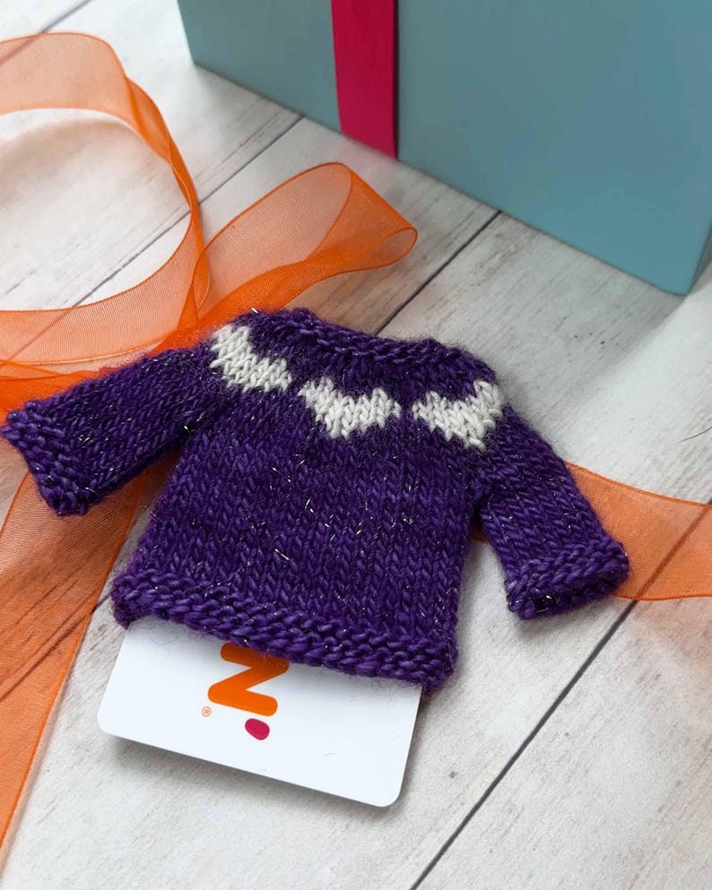 A purple miniature hand knit sweater used as a gift card holder.
