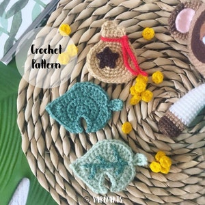 Puede incluir: Patrón de crochet para una hoja verde, una bolsa marrón con una cuerda roja y una estrella, y una pila de monedas amarillas. El patrón se llama "Crochet Pattern".