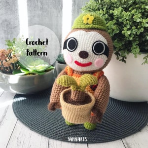 Puede incluir: Juguete de amigurumi de perezoso tejido a crochet sosteniendo una planta en maceta. El perezoso lleva un sombrero verde con una flor amarilla. El juguete es marrón, naranja, verde y blanco. El texto "Crochet Pattern" es visible en la imagen.
