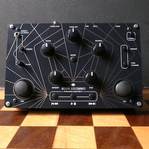 May include: Black and gold electronic music sampler with knobs, buttons, and a screen. The text on the screen reads "MELTED ELECTRONICS STRANGE LOOP MK II".