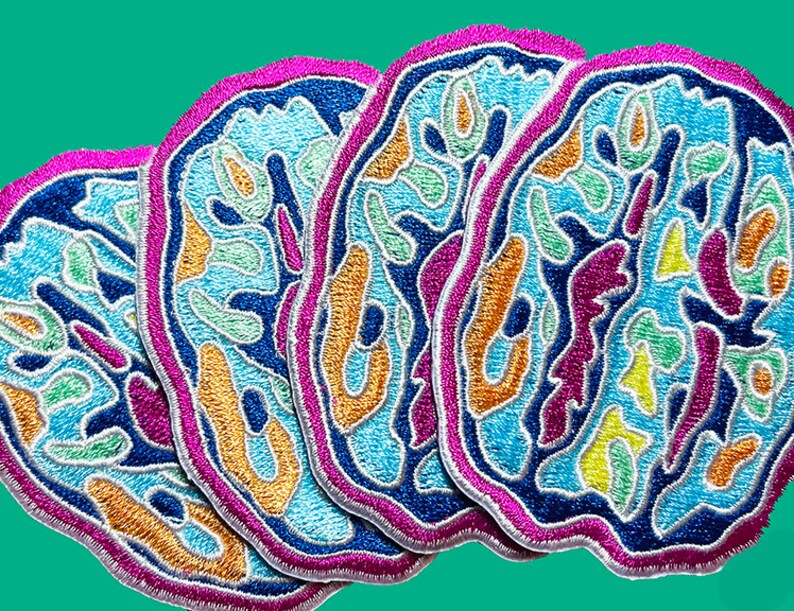 May include: Four embroidered patches in the shape of a brain, each with a different color scheme. The patches are blue, green, yellow, and orange with a white outline. The patches are layered on top of each other.