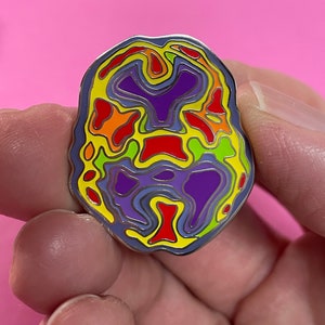 May include: A rainbow coloured enamel pin shaped like a brain. The pin has a silver outline and is detailed with a variety of colours, including red, orange, yellow, green, blue, and purple.