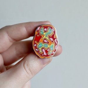 Könnte beinhalten: Eine farbige Emaille-Anstecknadel in Form eines Gehirns mit roten, orangen, gelben, grünen, blauen und rosa Wirbeln.