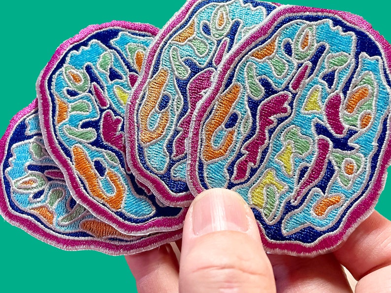 May include: Four colorful embroidered patches with a swirling, abstract design in shades of blue, pink, orange, yellow, and green. The patches are layered on top of each other and have a pink, white, and blue border.