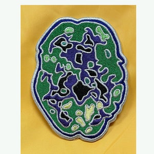 May include: An embroidered patch shaped like a brain, featuring green, purple and black colours. The patch has a silver outline.