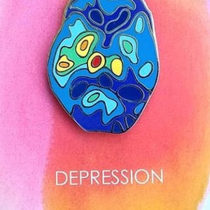 Op de afbeelding: Een blauwe en gele emaille pin met een gestileerd brein met de tekst "DEPRESSION" en "NEURO BLOOMS" eronder. De pin is een samenwerking tussen Leslie Holt en Shiny Apple Studio.