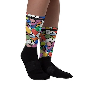 May include: A pair of black socks with a colourful pattern of pills on the upper part of the socks. The pattern is a mix of red, orange, yellow, green, blue, and purple pills.