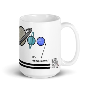May include: A white ceramic mug featuring a graphic of planets with rings, including Saturn, Uranus, and Neptune. An arrow points to a small dot with the text "It's complicated." The text "NERDY SCIENCE STUFF" is printed near the handle.