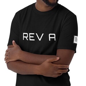 May include: A black short-sleeved t-shirt featuring the white text REV A printed across the chest. A small square white label with black text reading NERDY SCIENCE STUFF is attached to the edge of the left sleeve. The shirt has a crew neckline.