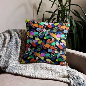 May include: A black cushion with a colourful pattern of pills and capsules. The cushion is made of soft fabric and has a zip closure.