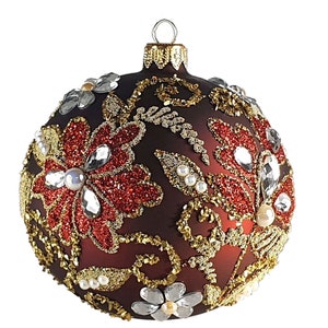 May include: A dark brown Christmas ornament with a floral design. The ornament is decorated with red glitter, gold glitter, and clear rhinestones.