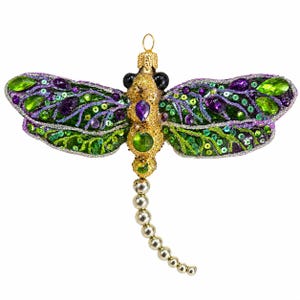 May include: A dragonfly ornament featuring a gold glittered body with purple and green faceted gems. The wings are decorated with green and purple sequins and glittered veins. A silver beaded tail extends downward from the main body.