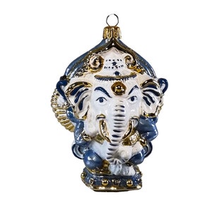May include: Ornament shaped like the Hindu deity Ganesha, featuring a white elephant head with blue and gold accents. The ornament has a loop for hanging and is designed with intricate details.