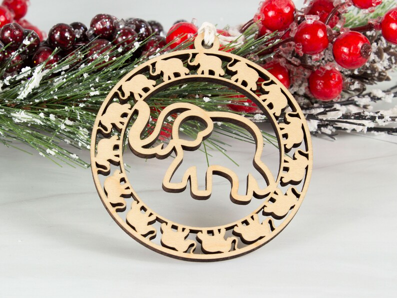 May include: A wooden Christmas ornament shaped like a circle with a large elephant cutout in the center. The elephant is surrounded by a ring of smaller elephants.