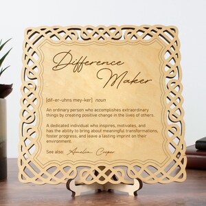 May include: Wooden plaque with a Celtic knot border and the word "Difference Maker" in cursive script. The plaque defines the word as "An ordinary person who accomplishes extraordinary things by creating positive change in the lives of others." The plaque also includes the text "See also. Amelia Cooper."