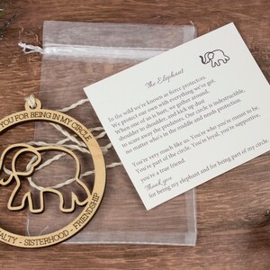Op de afbeelding: Houten ornament met een uitgesneden olifantontwerp. De ornament is rond en heeft de tekst "Thank you for being in my circle" en "Love - Loyalty - Sisterhood - Friendship" rond de olifant. De ornament wordt geleverd met een kleine kaart met de tekst "The Elephant" en een gedicht over olifanten.