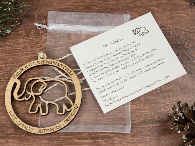 Op de afbeelding: Houten ornament met een uitgesneden olifantontwerp. De ornament is rond en heeft de tekst "Thank you for being in my circle" en "Love - Loyalty - Sisterhood - Friendship" rond de olifant. De ornament wordt geleverd met een kleine kaart met de tekst "The Elephant" en een gedicht over olifanten.