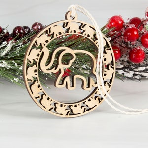 May include: A wooden Christmas ornament shaped like a circle with a large elephant cutout in the center. The ornament is decorated with smaller elephant cutouts around the edge.