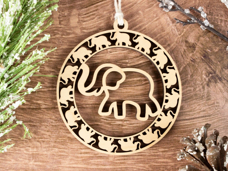 May include: A wooden Christmas ornament shaped like a circle with a large elephant cutout in the center. The elephant is surrounded by a ring of smaller elephant cutouts.