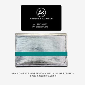May include: A silver wallet with a teal elastic band and the text "ANDERS & KOMISCH". Above the wallet is a black card with the same logo and text, including "RFID + NFC Blocker Card".