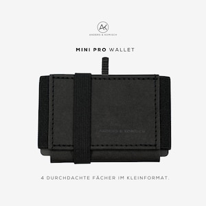 Könnte beinhalten: Schwarzes Mini Pro Portemonnaie mit schwarzem Gummiband. Das Portemonnaie trägt die Aufschrift "ANDERS & KOMISCH" und "MINI PRO WALLET". Das Bild enthält auch den Text "4 DURCHDACHTE FÄCHER IM KLEINFORMAT."