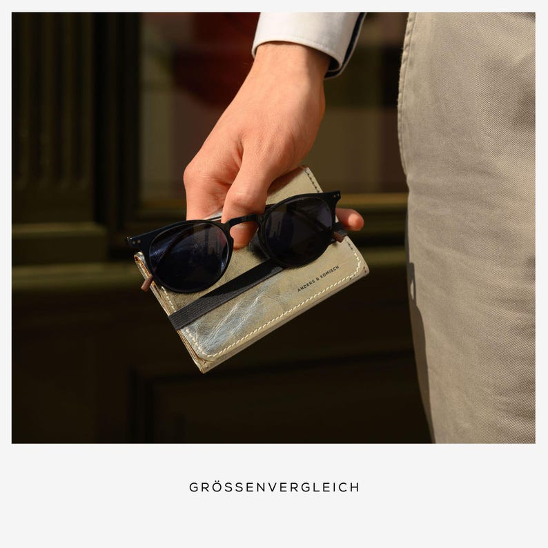 May include: Black sunglasses with round frames rest on a light-colored leather wallet held in a hand. The wallet has a black elastic band and the text "ANDERS & KOMISCH". The image also includes the text "GR&Ouml;SSENVERGLEICH".