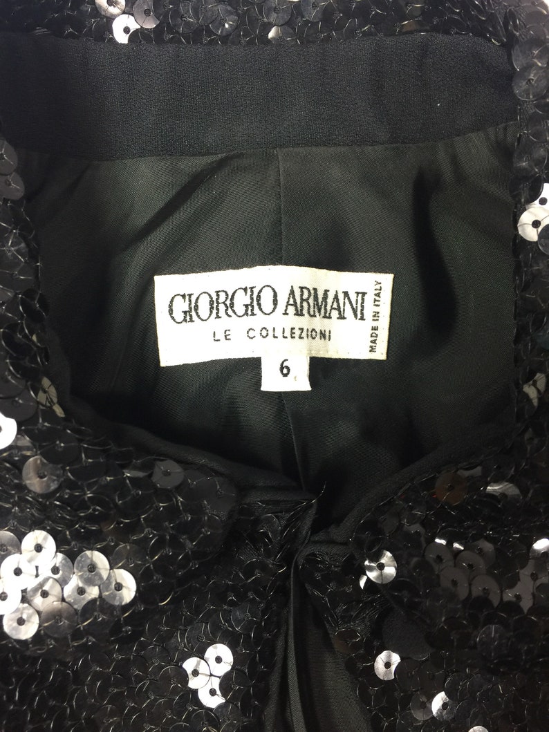 May include: Black sequined top with a label that reads "Giorgio Armani Le Collezioni Made in Italy" and a size tag that says "6".