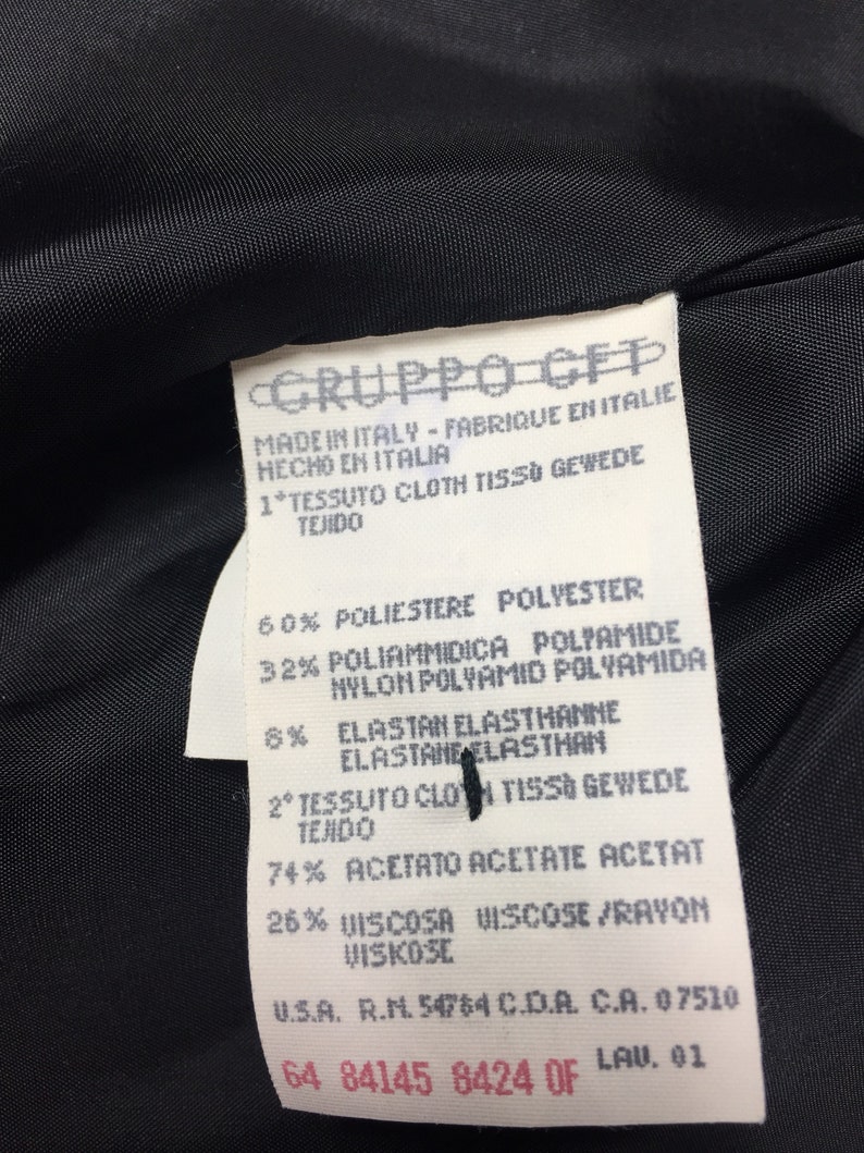 May include: A white tag with black text detailing the fabric composition of a garment. The tag reads "GRUPPO CEP", "Made in Italy - Fabrique en Italie - Hecho en Italia", "1* Tessuto Cloth tissu Gewebe Tejido", "60% Poliestere Polyester", "32% Poliammidica Polyamide Nylon Polyamid Polyamida", "6% Elastan Elasthanne Elastane Elasthan", "2&ordm; Tessuto Cloth Tissu Gewebe Tejido", "74% Acetato Acetate Acetat", "26% Viscosa Viscose/Rayon Viskose", "U.S.A. R.N. 54764 C.D.A. C.A. 07510", "64 84145 8424 OF LAU. 01".