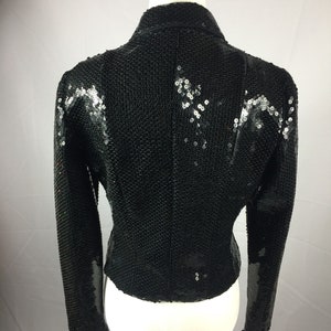 May include: A black sequined jacket with long sleeves. The jacket has a fitted silhouette and a high collar.