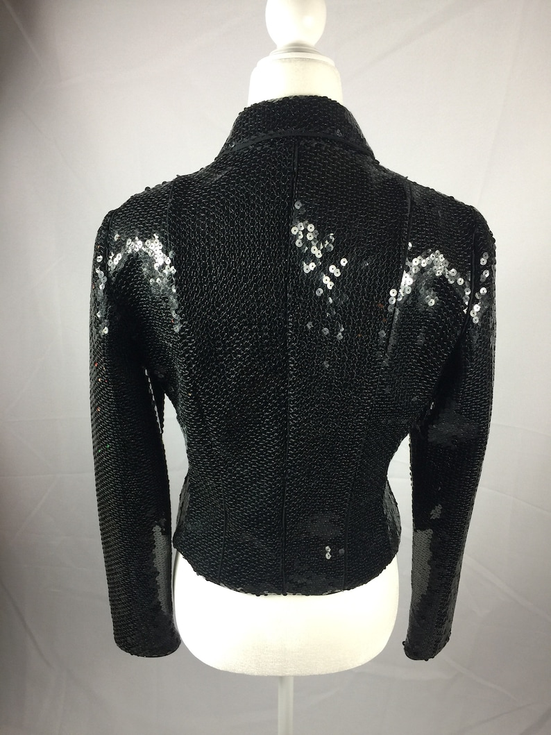 May include: A black sequined jacket with long sleeves. The jacket has a fitted silhouette and a high collar.