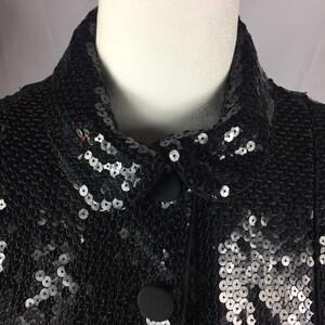 May include: A black sequined jacket with a collar and button closure. The sequins are silver and black.