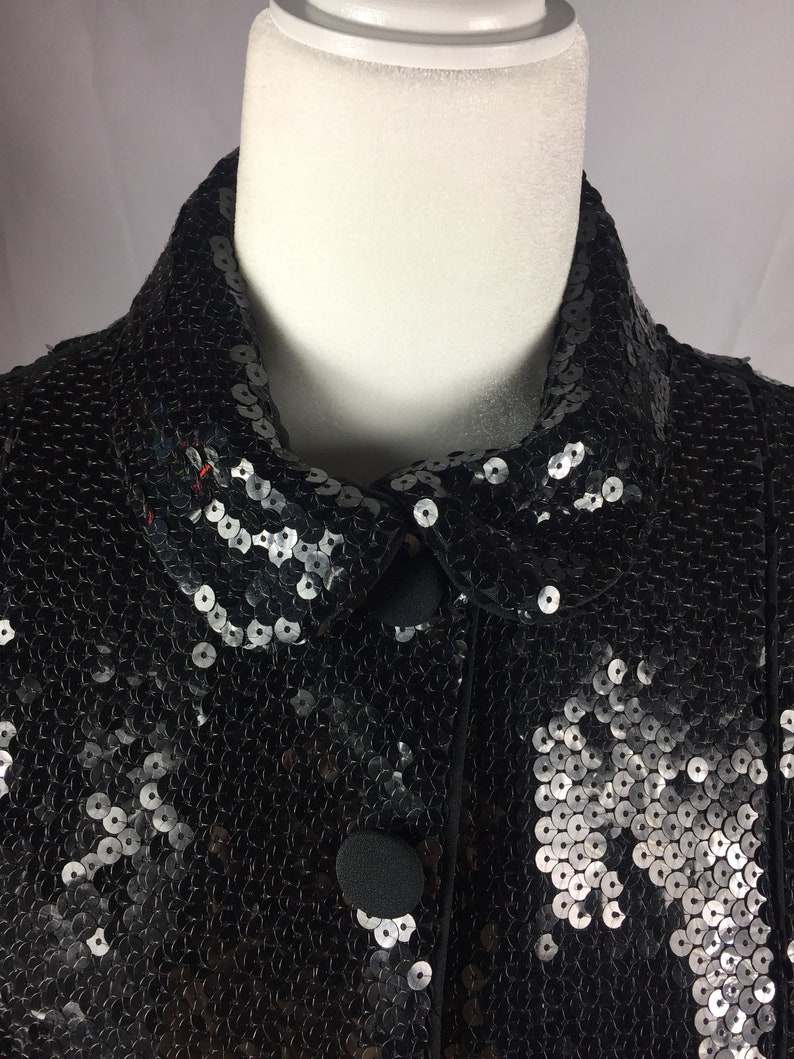 May include: A black sequined jacket with a collar and button closure. The sequins are silver and black.
