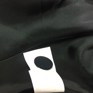 May include: A close-up of a black fabric with a white label attached. The label has a black circle in the center.