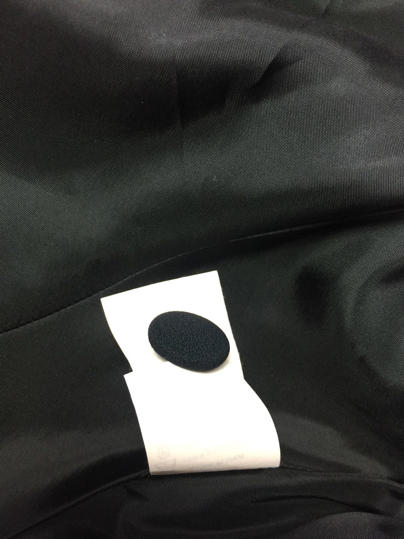 May include: A close-up of a black fabric with a white label attached. The label has a black circle in the center.