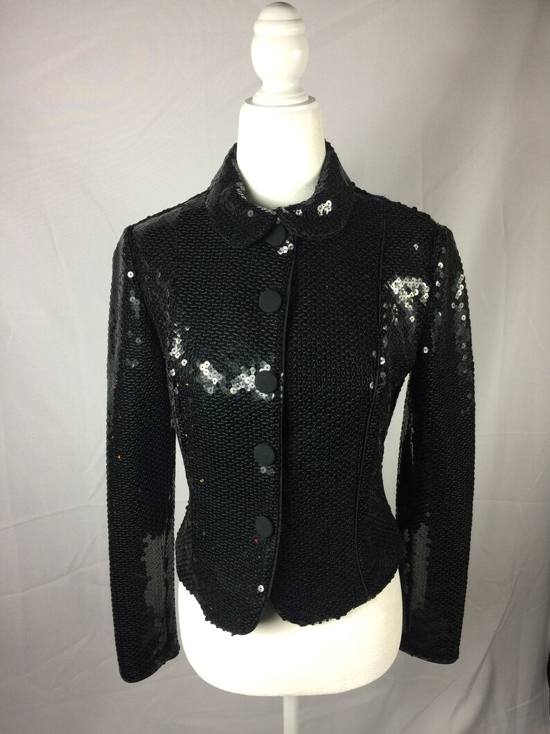 May include: A black sequined jacket with a button closure and long sleeves.