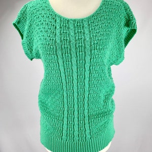 May include: A green knitted sweater with short sleeves and a round neckline. The sweater has a textured pattern.